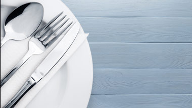 plate setting with napkin, fork, knife & spoon on a blue wood background
