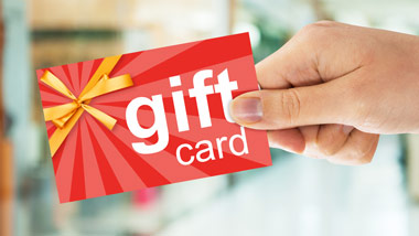 woman holding a gift card, gift card has red starburst pattern, a gold ribbon and says: "gift card" in white text